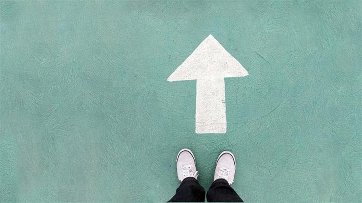 photo of white arrow drawn on green sidewalk looking down on person's feet at its base