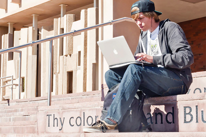 student with laptop sitting on steps of university building