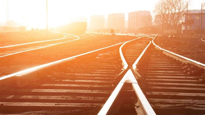 ground-level photo of merging railroad tracks backlit by setting sun