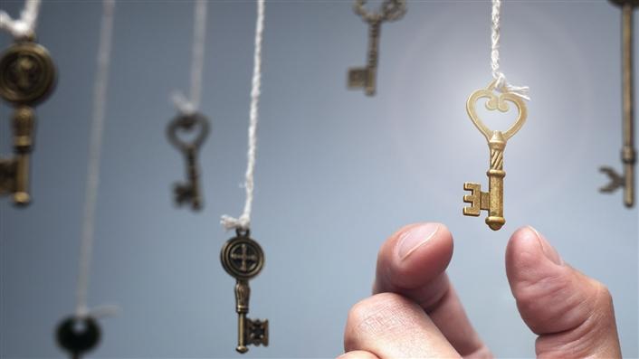 photo of old-fashioned keys suspended on strings and a man's hand reaching for one of them
