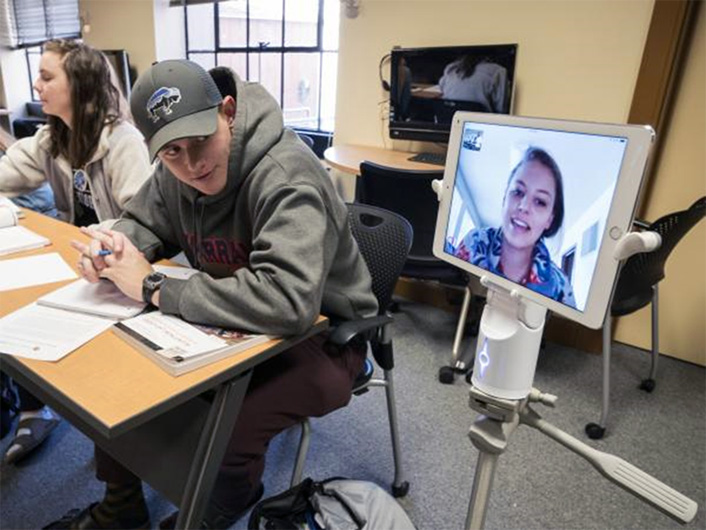 Student in classroom interacts with remote student attending class via Kubi technology.