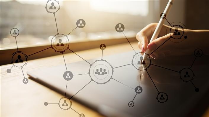 photo of a hand writing on a laptop with interconnected people icons overlaid on it