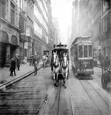 Street view of a horse drawn carriage next to a trolley car.