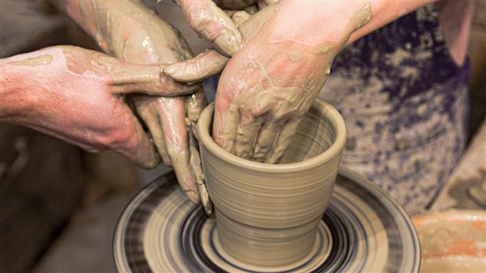 photo of several pairs of hands throwing a clay pot