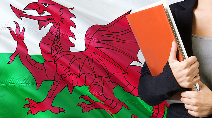 Young woman standing with the Wales flag in the background holding books.