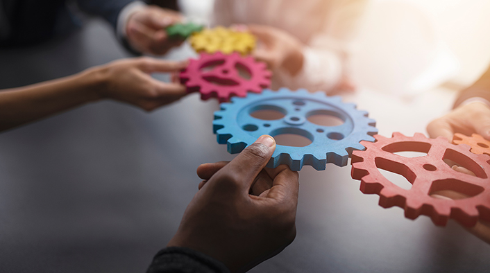 people holding together different colored mechanical gears/cogwheels