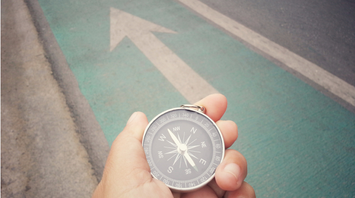 close up hand holding compass with paint arrow on road