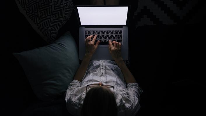 person lying on a couch in the dark using a laptop