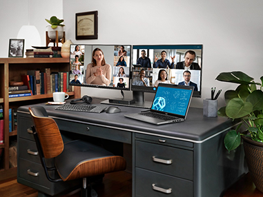 Desk with a laptop and two monitors showing an ongoing video conference.