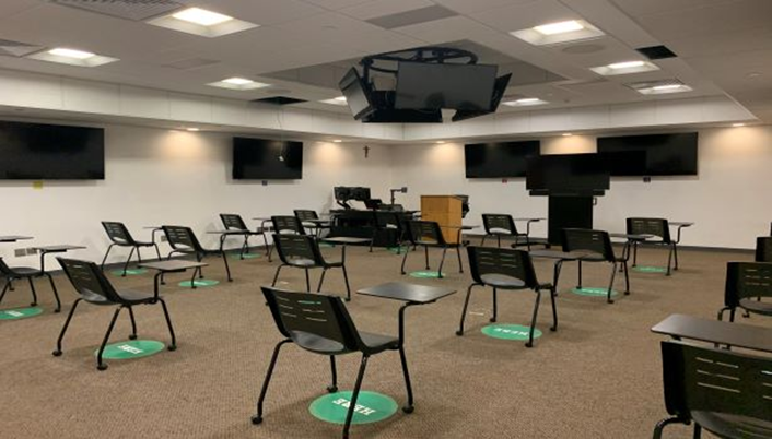 Individual chairs with attached desk spaced 6 feet apart in rows facing the front of a room