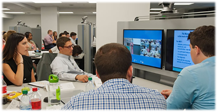 People sitting around a table looking at two monitors.