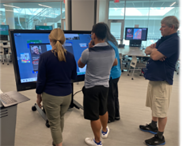 4 people standing in front of and looking at a large monitor