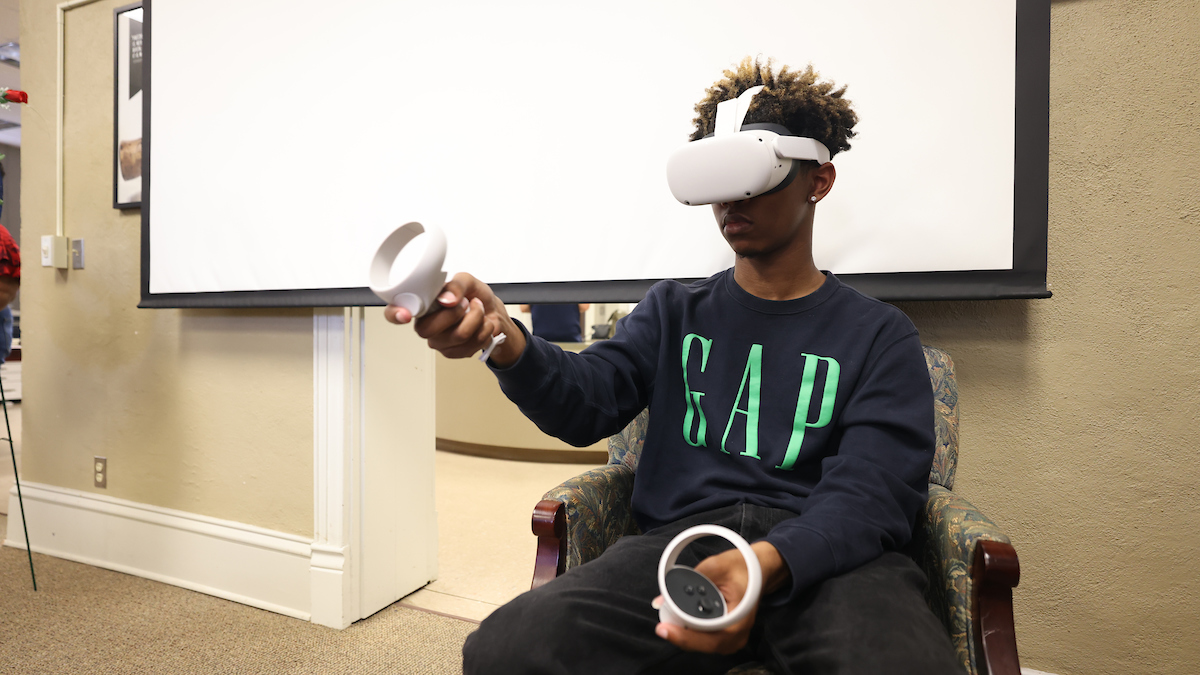 Photograph of a student wearing a VR headset and manipulating two handheld controllers. 