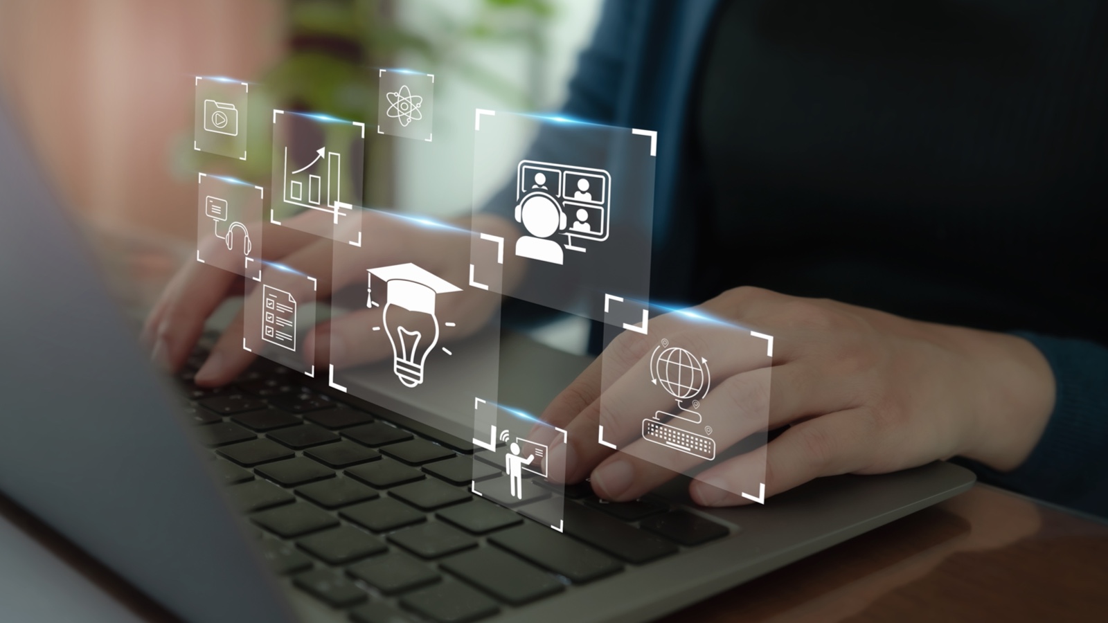 Hands on a laptop keyboard. Popping up above the keyboard are clear squares, each of which has an icon representing something to do with online education.