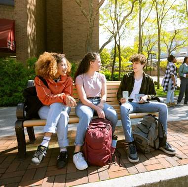 3 students sitting on a bench outside.