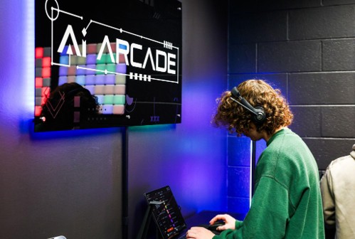 A college-aged person in a green sweater engages with music equipment under an