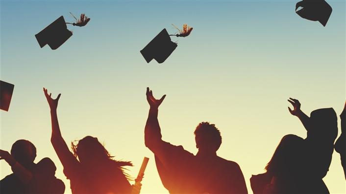 silhouette image of students throwing graduation caps into the air