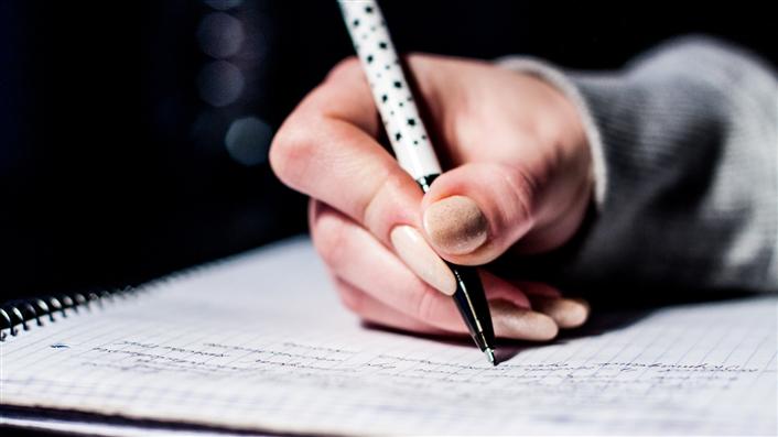 photo of hand holding a pen and writing in a notebook