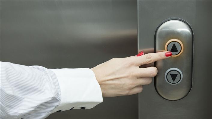 photo of woman's arm and finger pressing an elevator up button