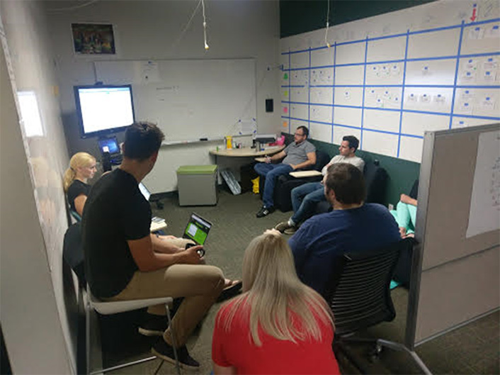 Looking into a room with a group of people sitting in a circle. Some have their backs to the camera.