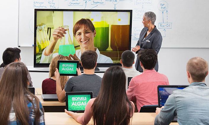 classroom of students watching a presentation on a screen at the front of the room.