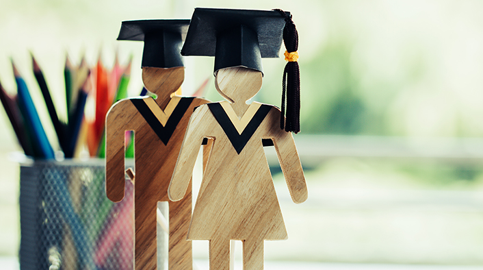 2 wooden figures wearing graduation caps and standing on an open textbook.