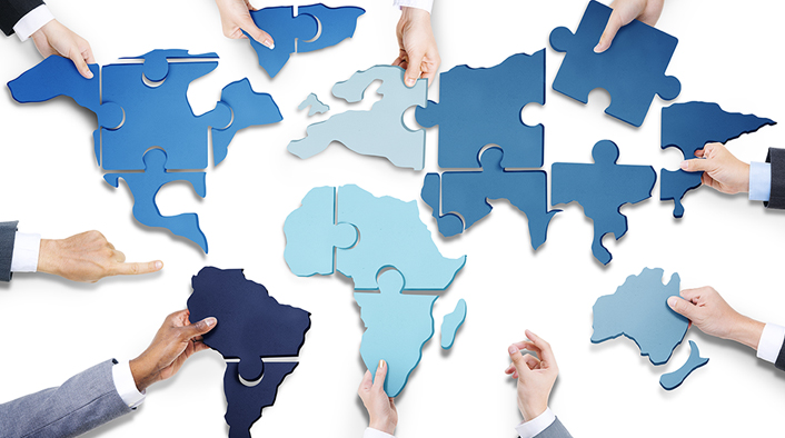 people assembling a jigsaw puzzle whose pieces form countries and continents of the world