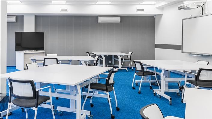 Panorama of modern college group study room with white desks, chairs, big tv screen and board 