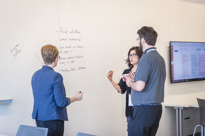 three Mosaic Fellows talking and drawing on a whiteboard