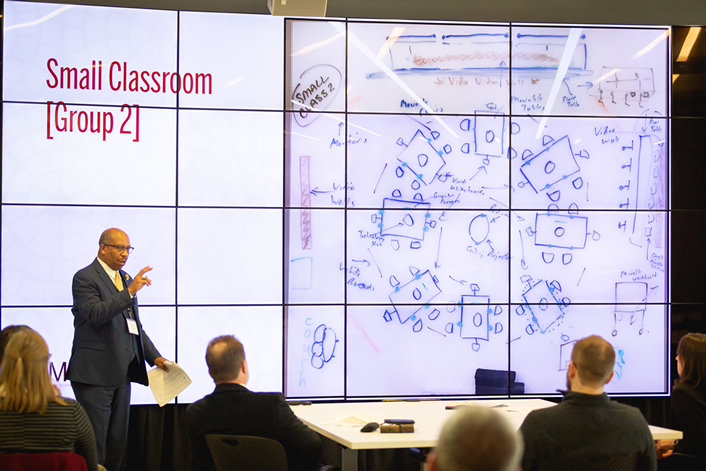 two Senior Fellows presenting to attendees using a large video screen