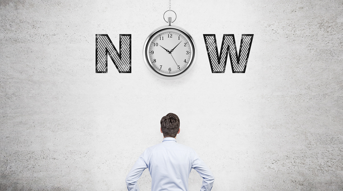 man looking up at the word NOW with a pocked watch suspended in place of the O