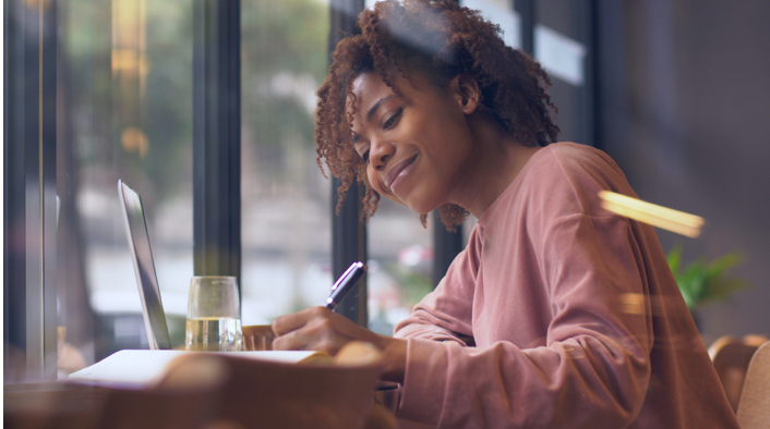 woman working at a laptop and writing in a notebook