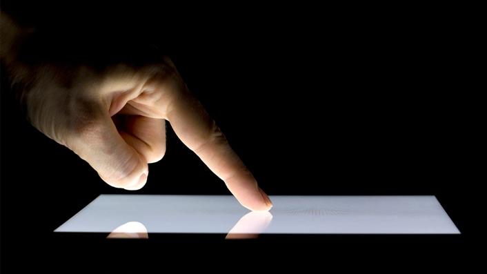 Close-up of an index finger pressing the screen of a pad device