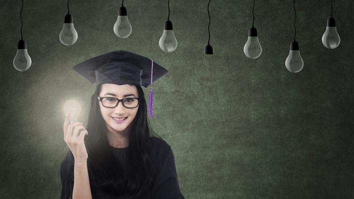 Female college student holding a lit lightbulb, many unlit lightbulbs hang above her