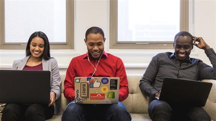 Three African-American individuals sitting on a couch with laptops