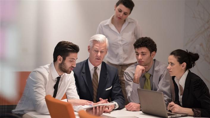 Group of five people sitting at a meeting table working on an iPad