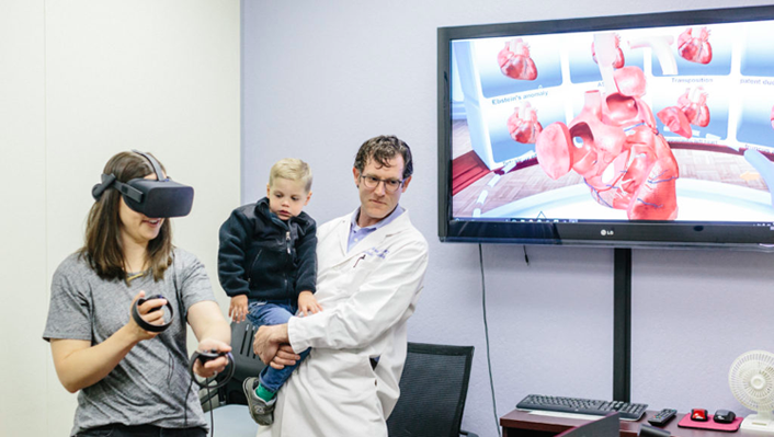 Dr. David Axelrod with KC Grewal, wearing a virtual reality headset, and her son Rowan, a patient at Stanford's Lucile Packard Children's Hospital.